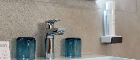 A bathroom sink with a modern faucet, two blue glass containers, and a hand sanitizer dispenser on the wall.