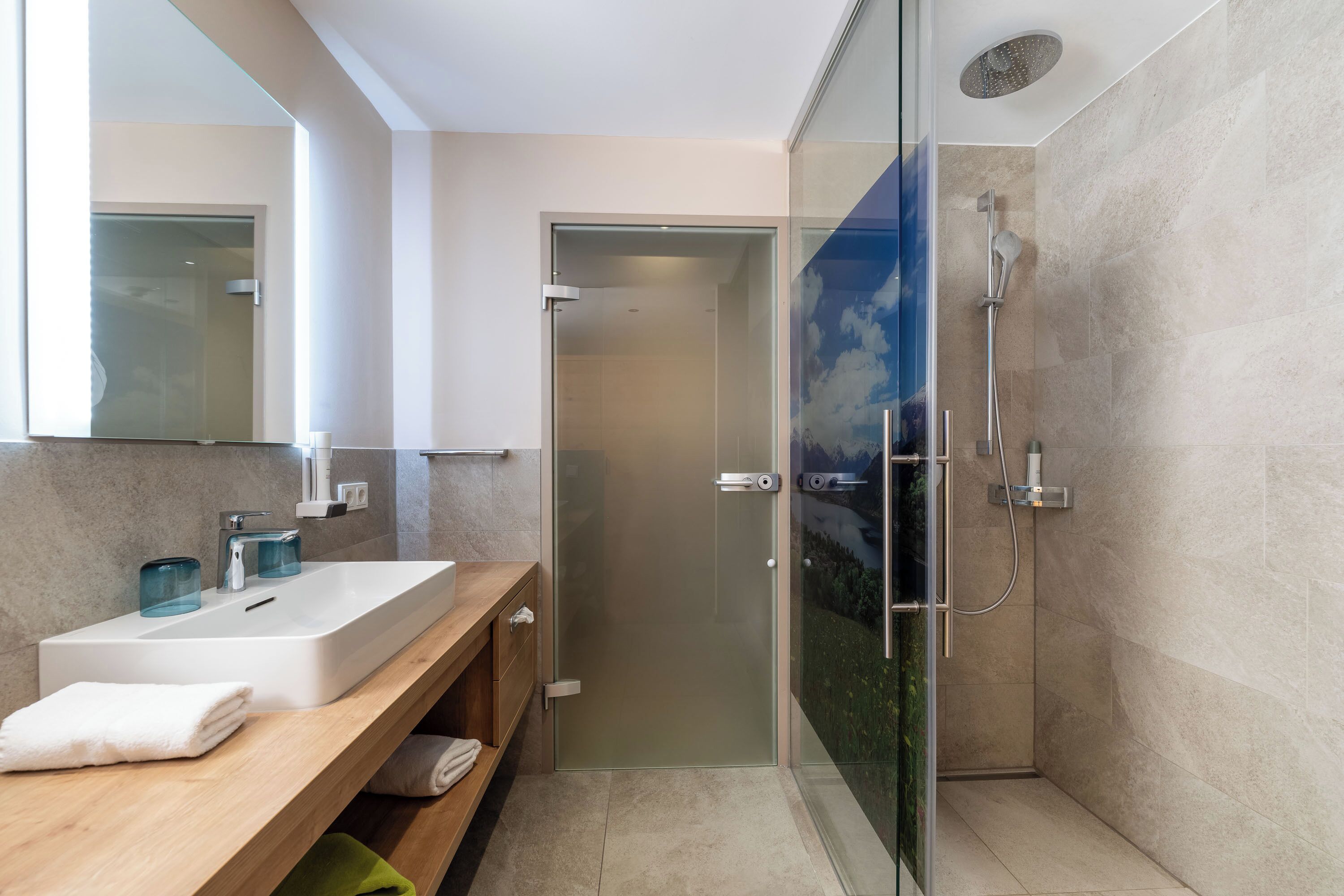 A modern bathroom with a glass-enclosed shower, a wooden vanity with a sink, and a large mirror.