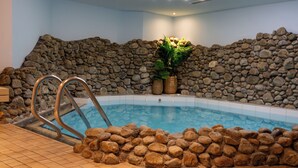 Une piscine intérieure avec un mur en pierre et une échelle permettant d’accéder à l’eau.