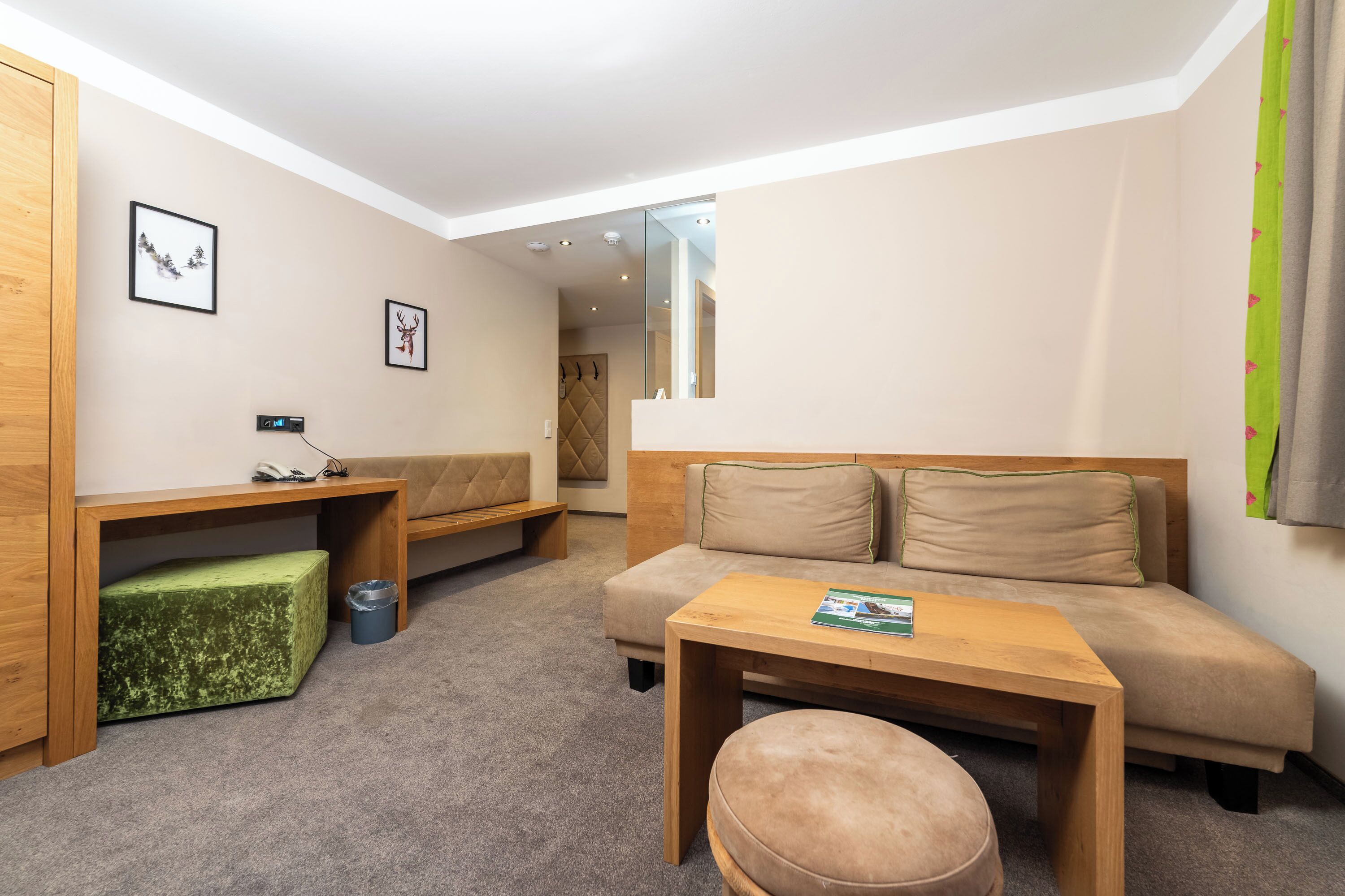 A modern, well-lit room with a sofa, a wooden table, and a green ottoman.