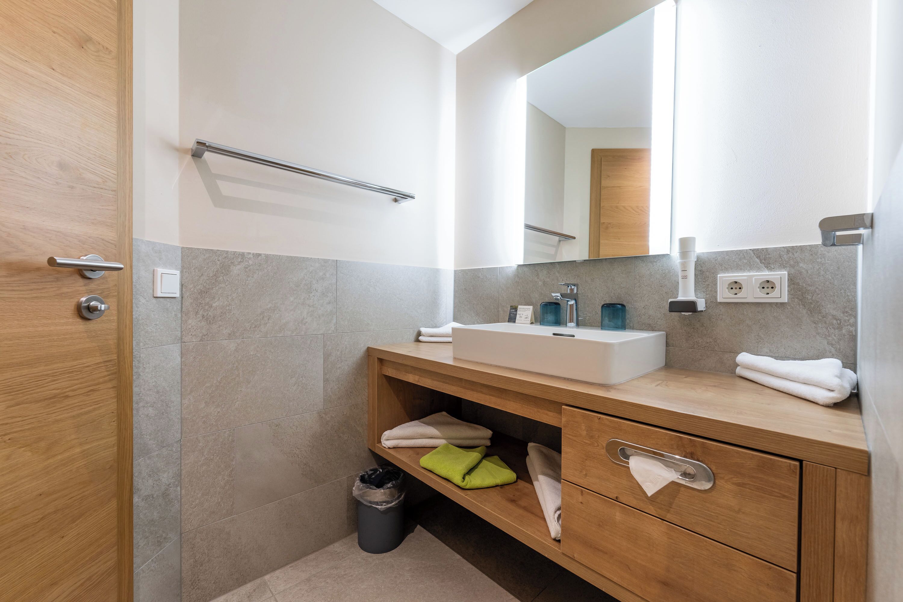 A modern bathroom with a wooden vanity, a mirror, and a towel rack.
