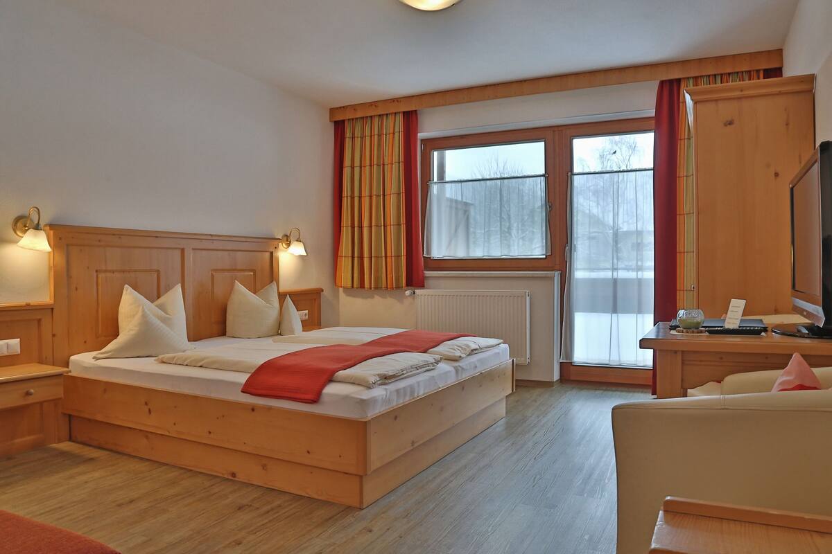 A bedroom with a wooden bed, a desk with a computer, and a television.