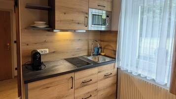 Une cuisine moderne avec des meubles en bois, un four à micro-ondes encastré, un évier et une fenêtre ornée de rideaux légers.