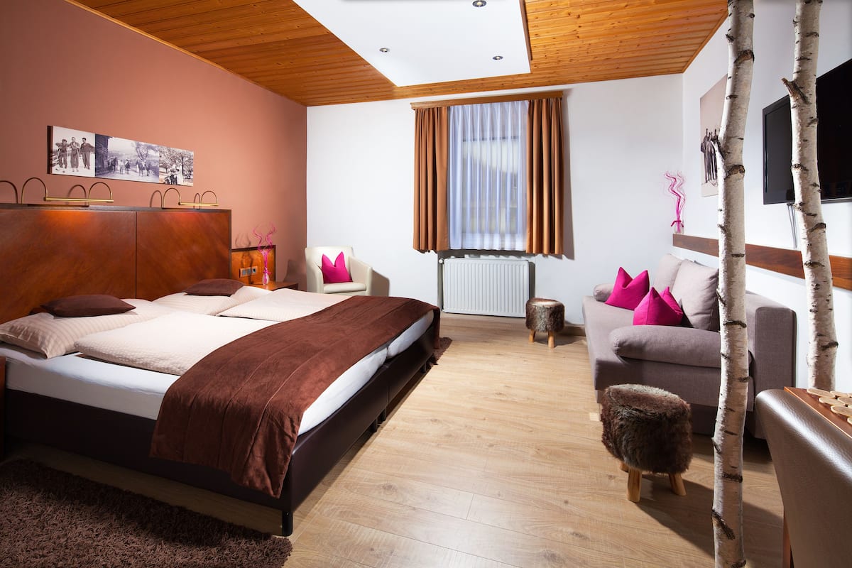 Un dormitorio moderno con una cama grande, un sofá, un taburete pequeño y un televisor montado en la pared.