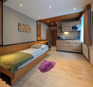 Quarto moderno com cama de madeira, pequeno espaço de cozinha e teto de madeira.