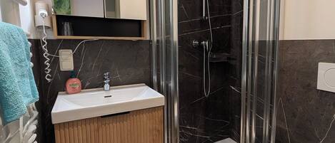 Un baño moderno con ducha de vidrio, tocador de madera, lavamanos blanco y retrete.