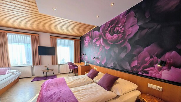 A modern hotel room with a large bed, a desk, and a vibrant flower mural on the wall.