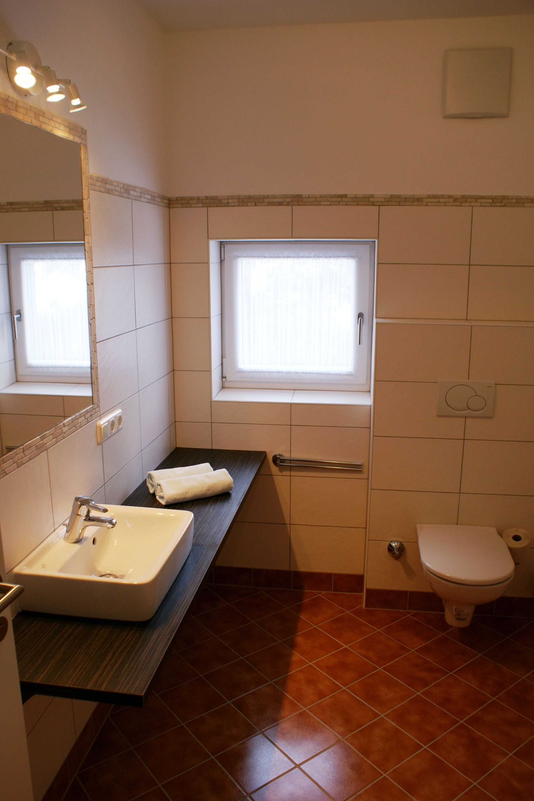 A bathroom with a sink, mirror, window, toilet, and a towel on the counter.