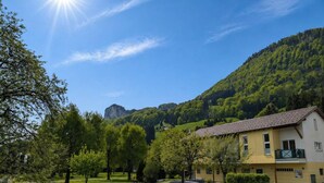 A residential building with a swimming pool, surrounded by greenery and mountains.