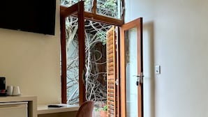 A bedroom with a bed, a desk, a chair, and a window with a view of trees. - Loloho Lodge (Cape Town)