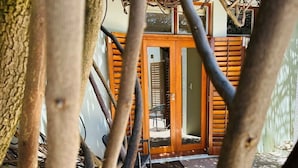 A wooden door with a glass panel, leading to a patio area with a chair and a small table. - Loloho Lodge (Cape Town)