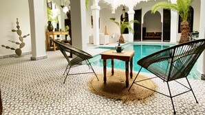 A courtyard with a pool, two chairs, a table, and a decorative plant. - Riad Fabiola et Spa By La Siredrah (Marrakech)