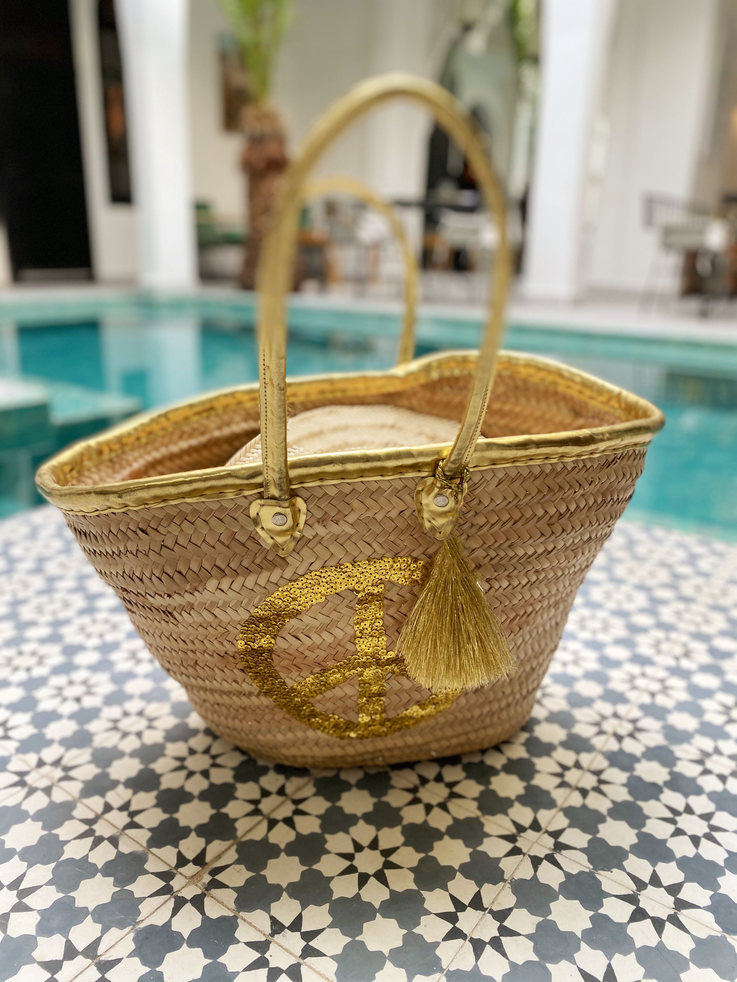 A woven basket with a golden handle and tassel, placed on a tiled floor with a geometric pattern.