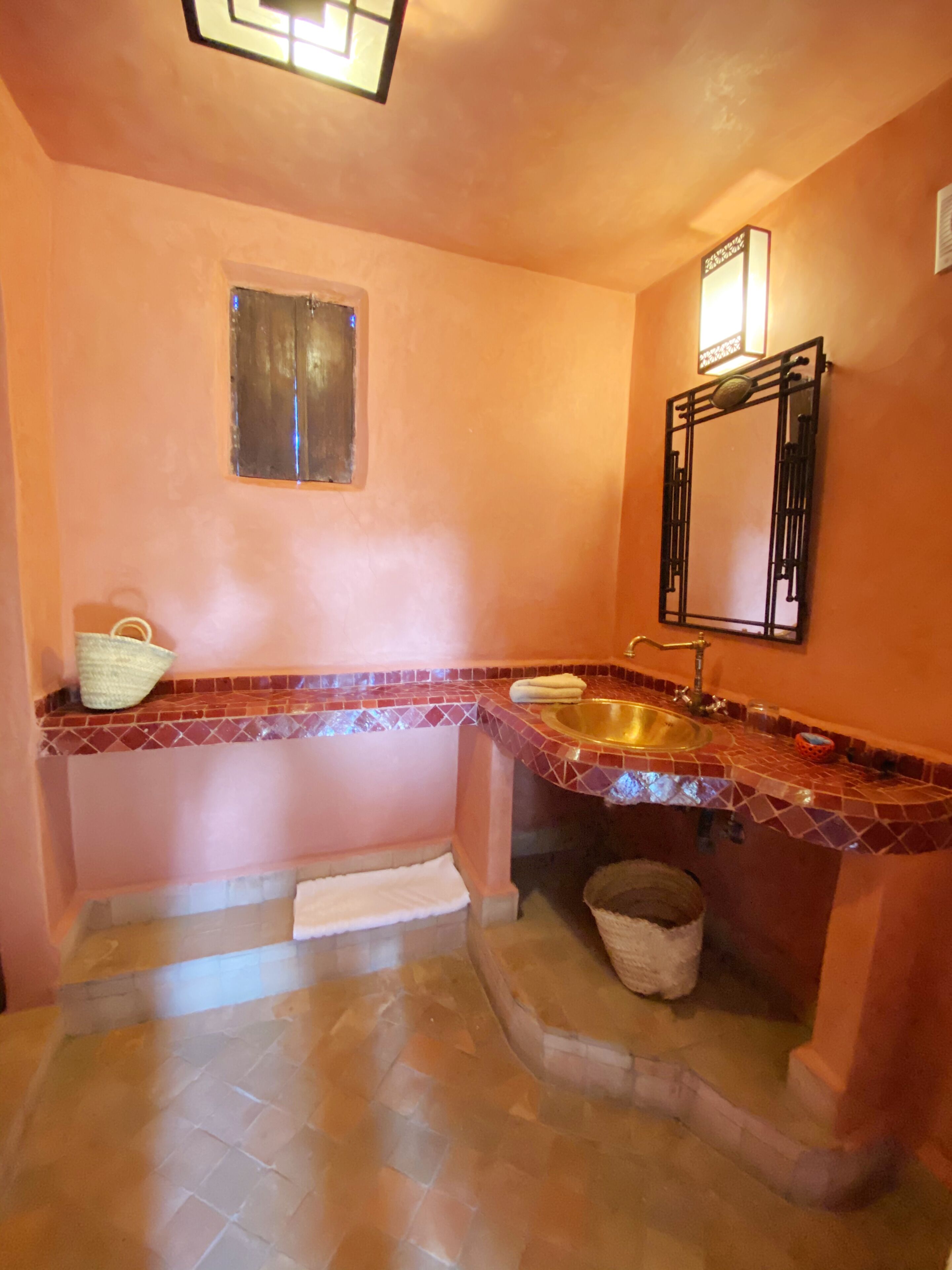 A bathroom with a tiled floor, a sink, a mirror, and a window.