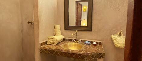 Un baño con suelo de baldosas, un lavabo con espejo, ducha y un perchero para toallas.
