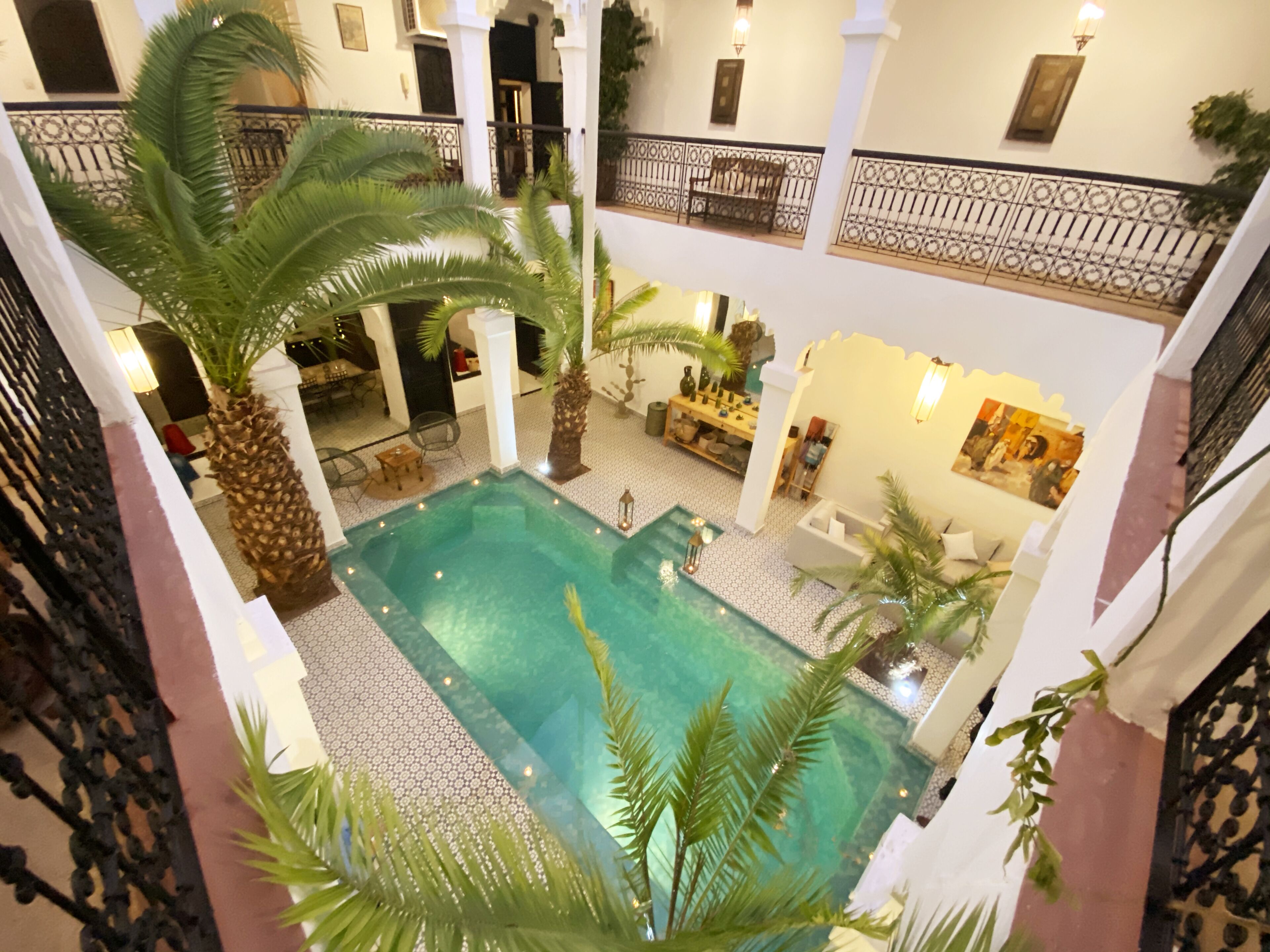 A spacious indoor swimming pool with a tiled floor, surrounded by palm trees and a seating area with chairs and a table.