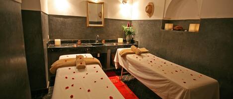 Un cuarto de spa con dos camillas, un espejo, un lavabo y un florero con flores.