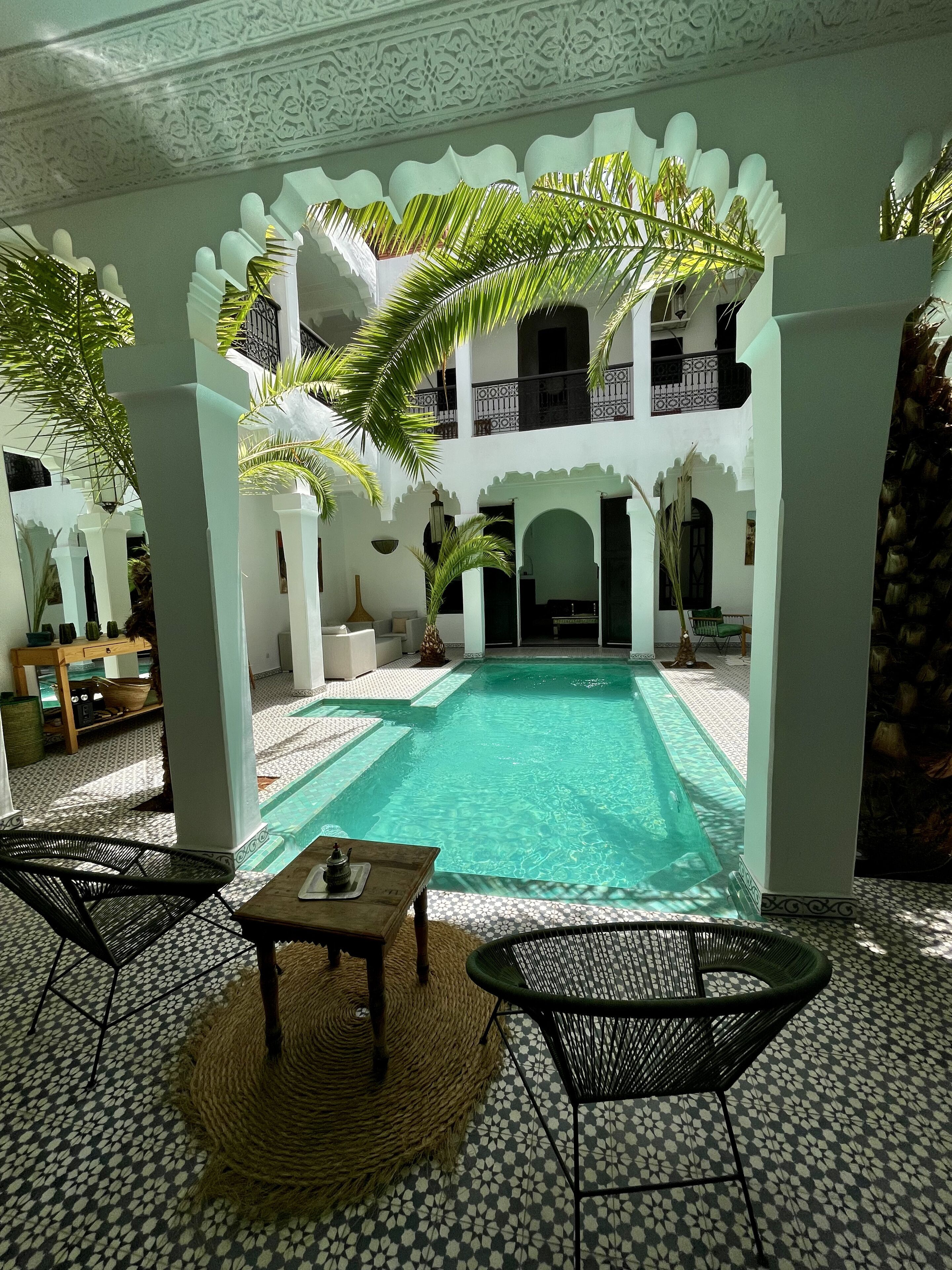 A pool area with a tiled floor, two chairs, a table, and a decorative plant.