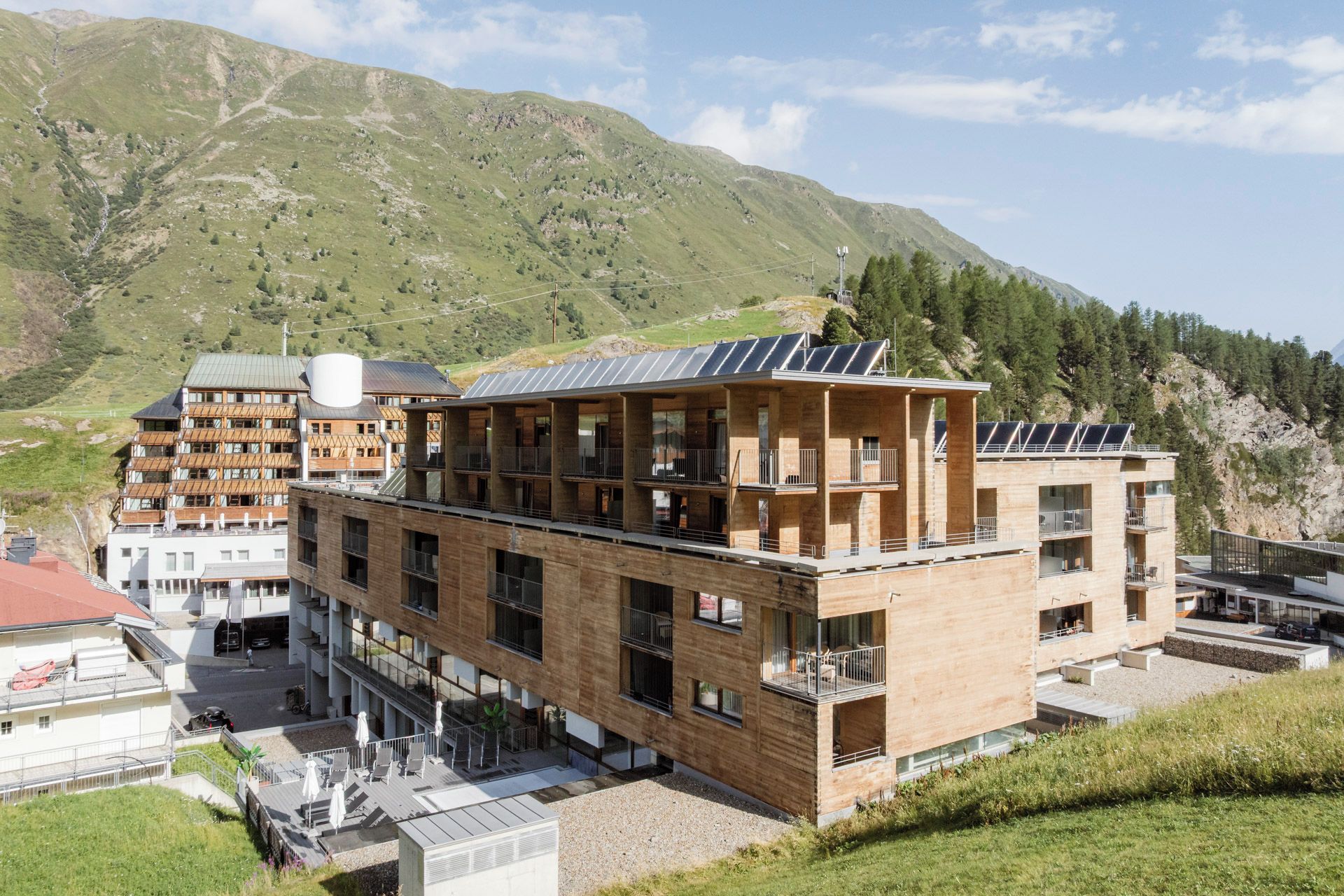 Ein modernes, mehrstöckiges Gebäude mit Balkonen, Solaranlagen und Bergblick.