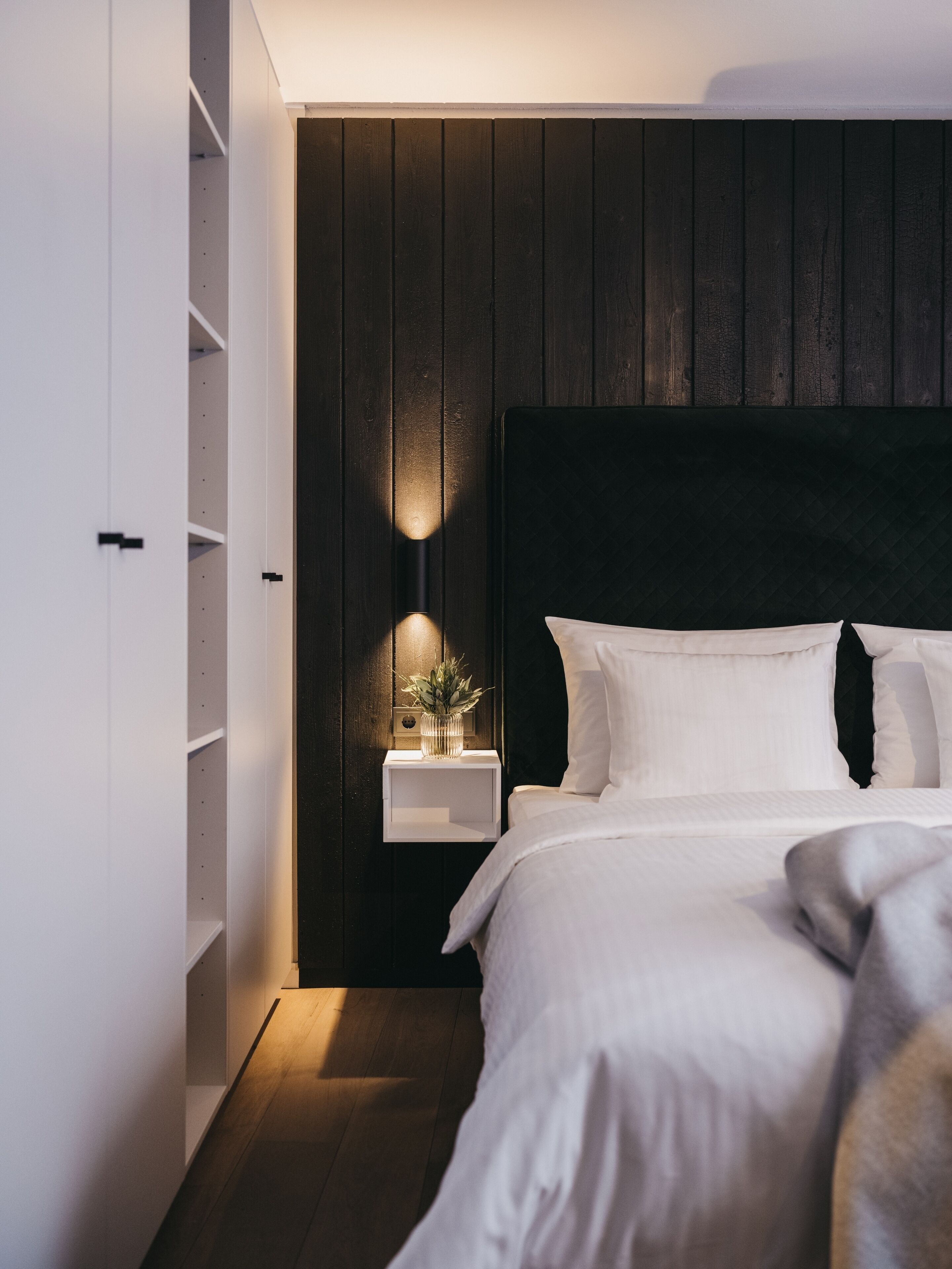 Une chambre à coucher avec une tête de lit en bois foncé, une table de chevet ornée d’une plante et un couvre-lit blanc.