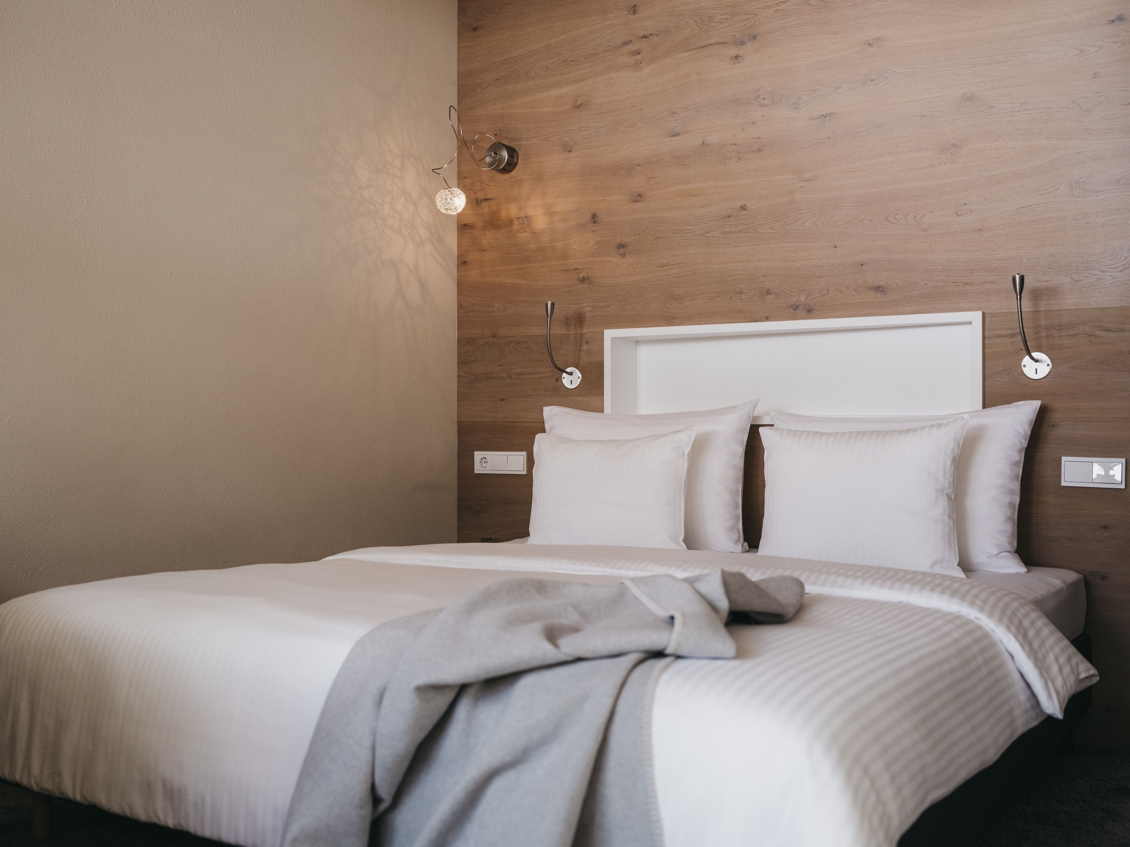 Een netjes opgemaakt bed met een wit hoofdeinde, een nachtkastje en een wandlamp.