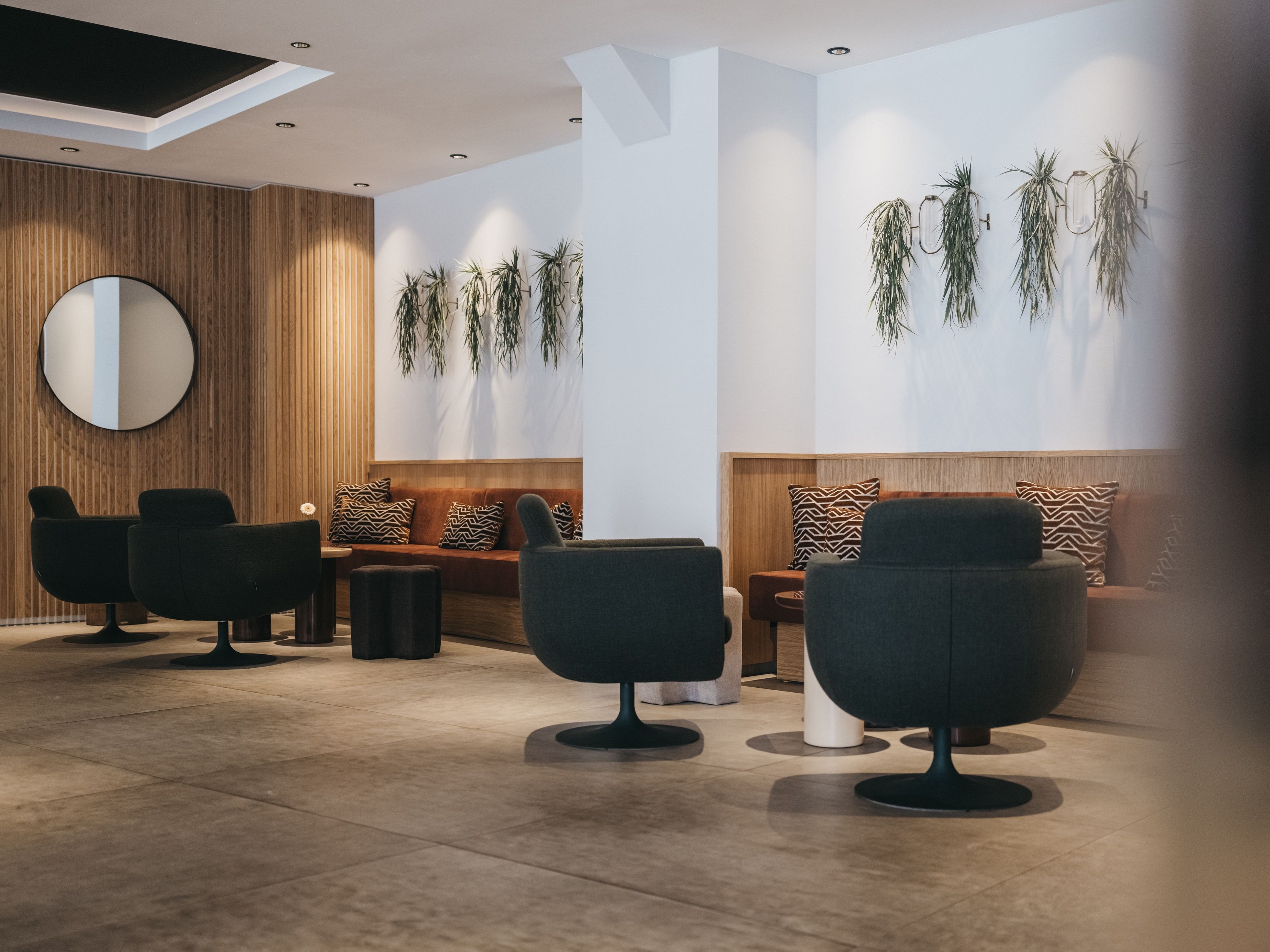 A modern interior with a seating area, a round mirror, and wall-mounted plants.