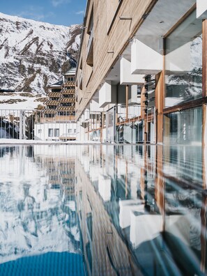 Un edificio moderno con una piscina reflectante en primer plano, rodeado de montañas nevadas.