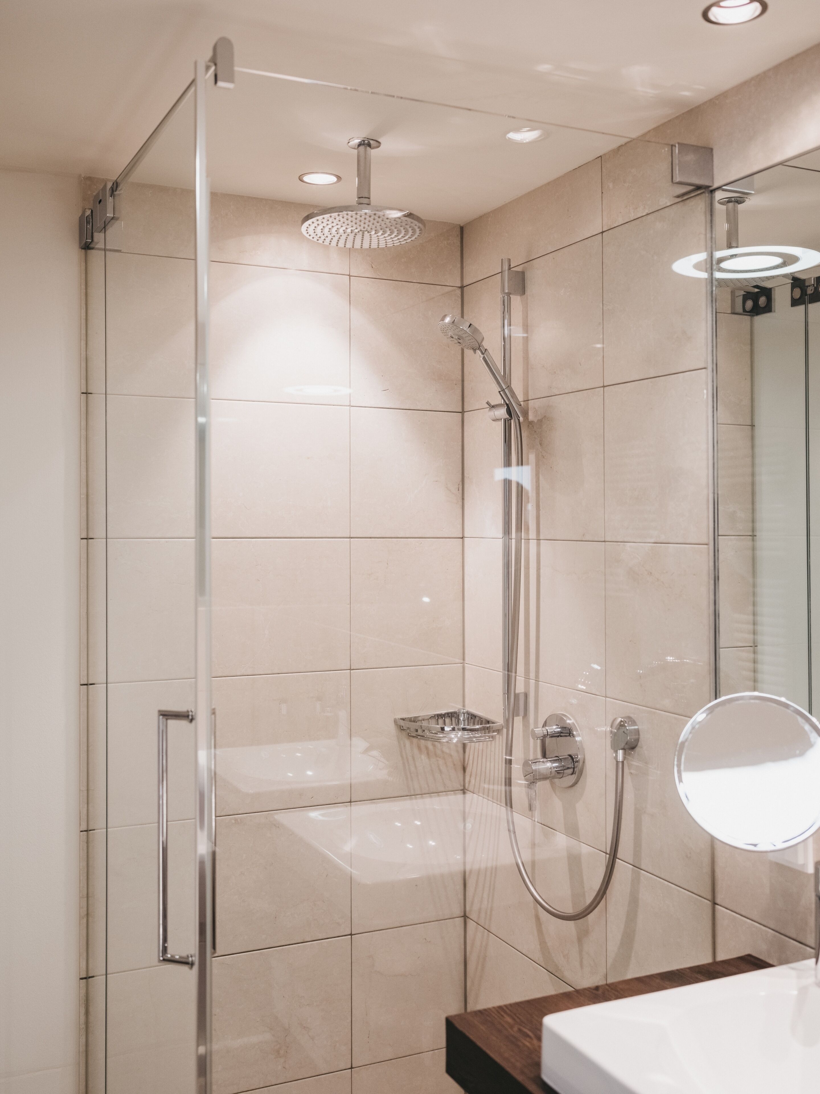 Une salle de bain moderne dotée d’une douche à parois de verre, d’un pommeau de douche à main, d’un robinet mural et d’un miroir rond.