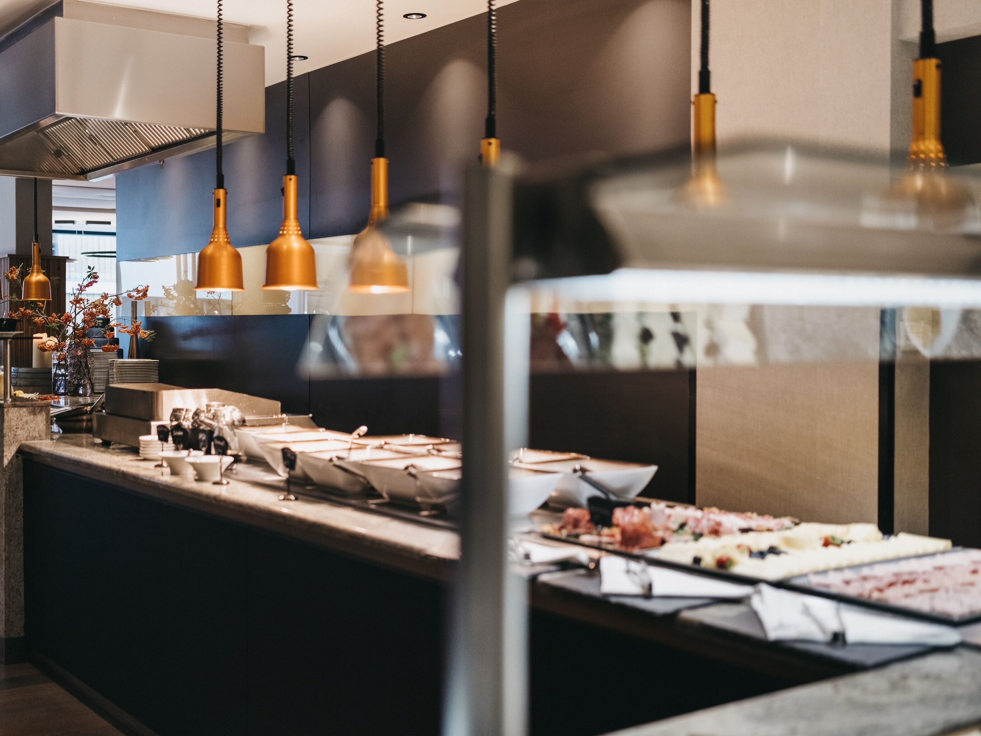 A modern kitchen with pendant lighting, a stainless steel range hood, and a buffet counter with various dishes.