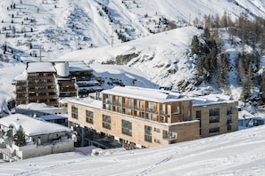 Un hôtel moderne à plusieurs étages, doté de grandes fenêtres et offrant une vue sur une piste de ski en arrière-plan.