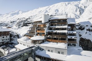 A multi-story hotel with a ski slope in the background, featuring a mix of modern and traditional architecture. - The Crystal VAYA Unique (Obergurgl)