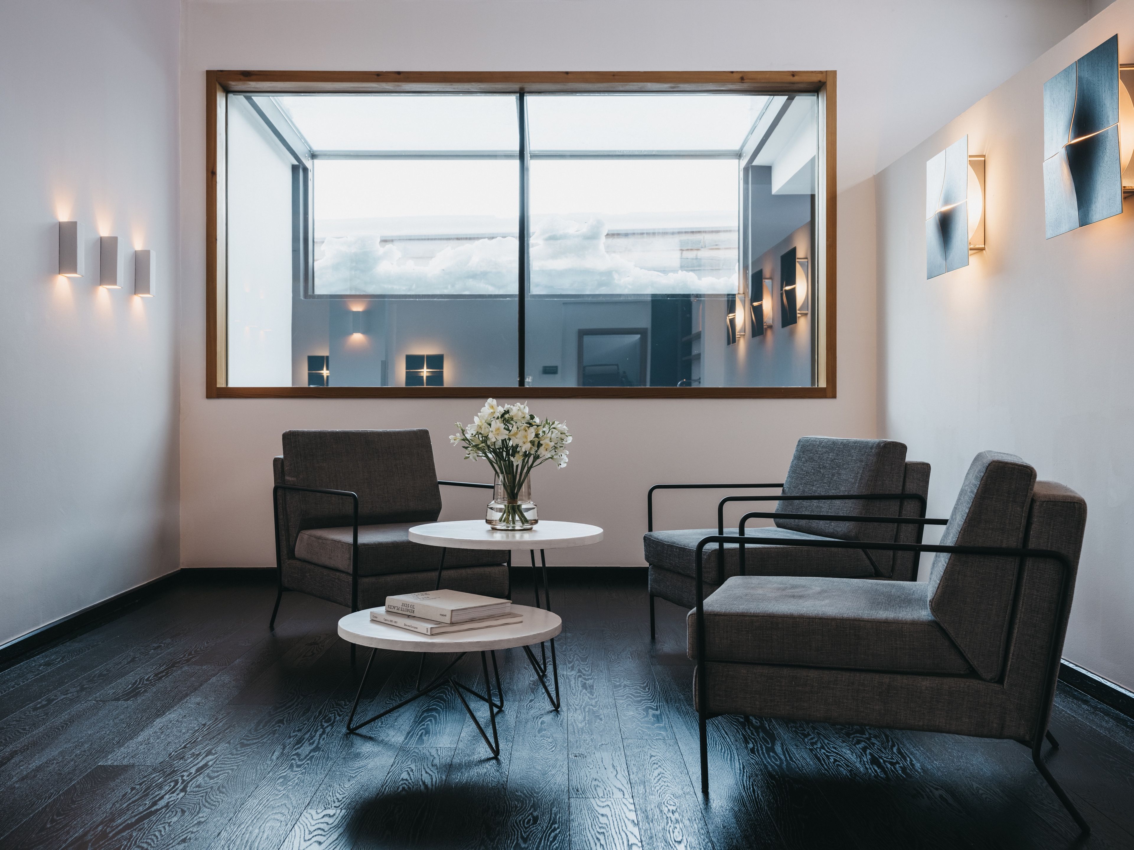 A modern room with a large window, two chairs, a small table, and a vase of flowers.