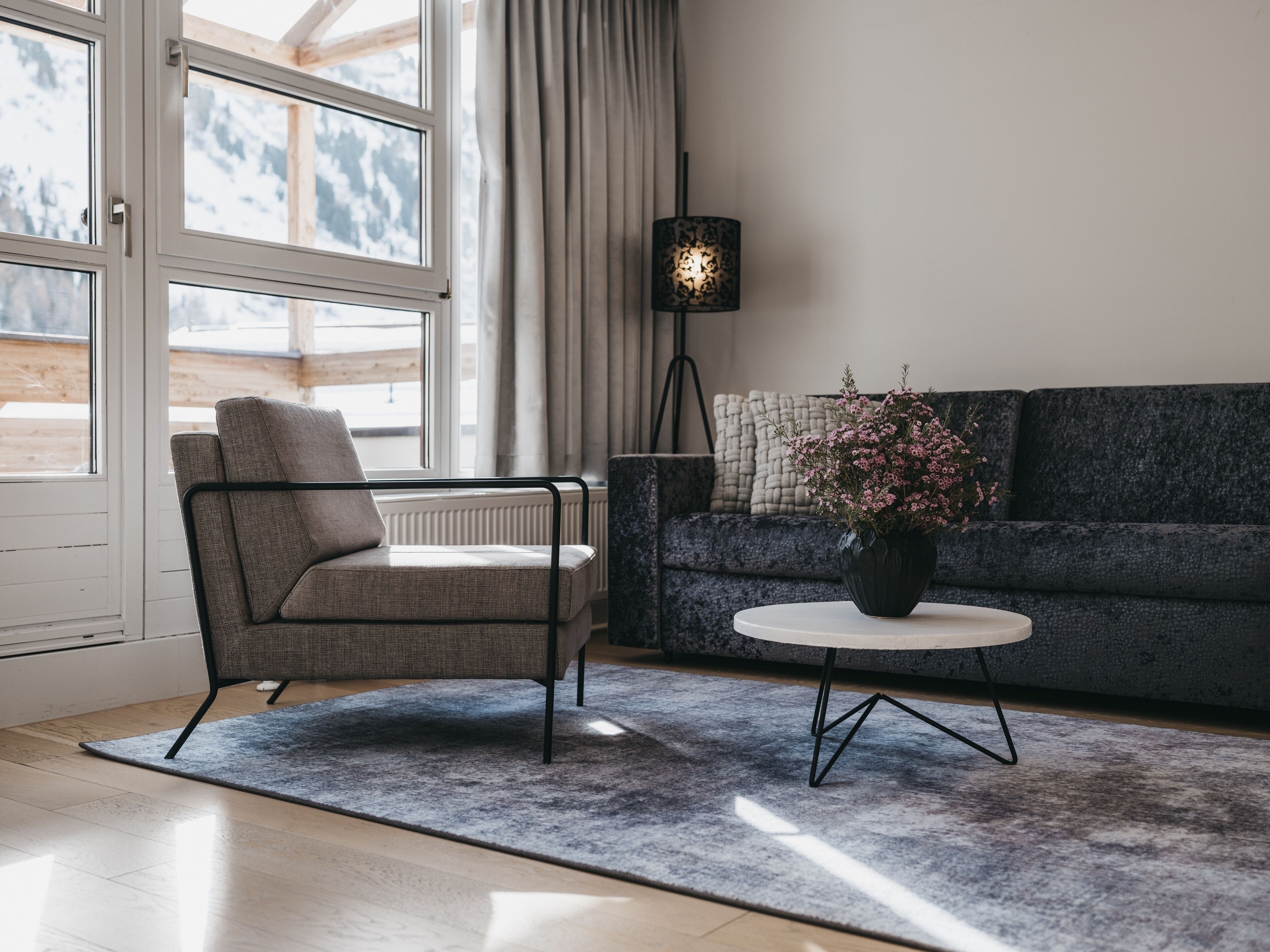 Ein modernes Wohnzimmer mit einer Couch, einem Sessel, einem kleinen Tisch mit einer Vase und einer Stehlampe.