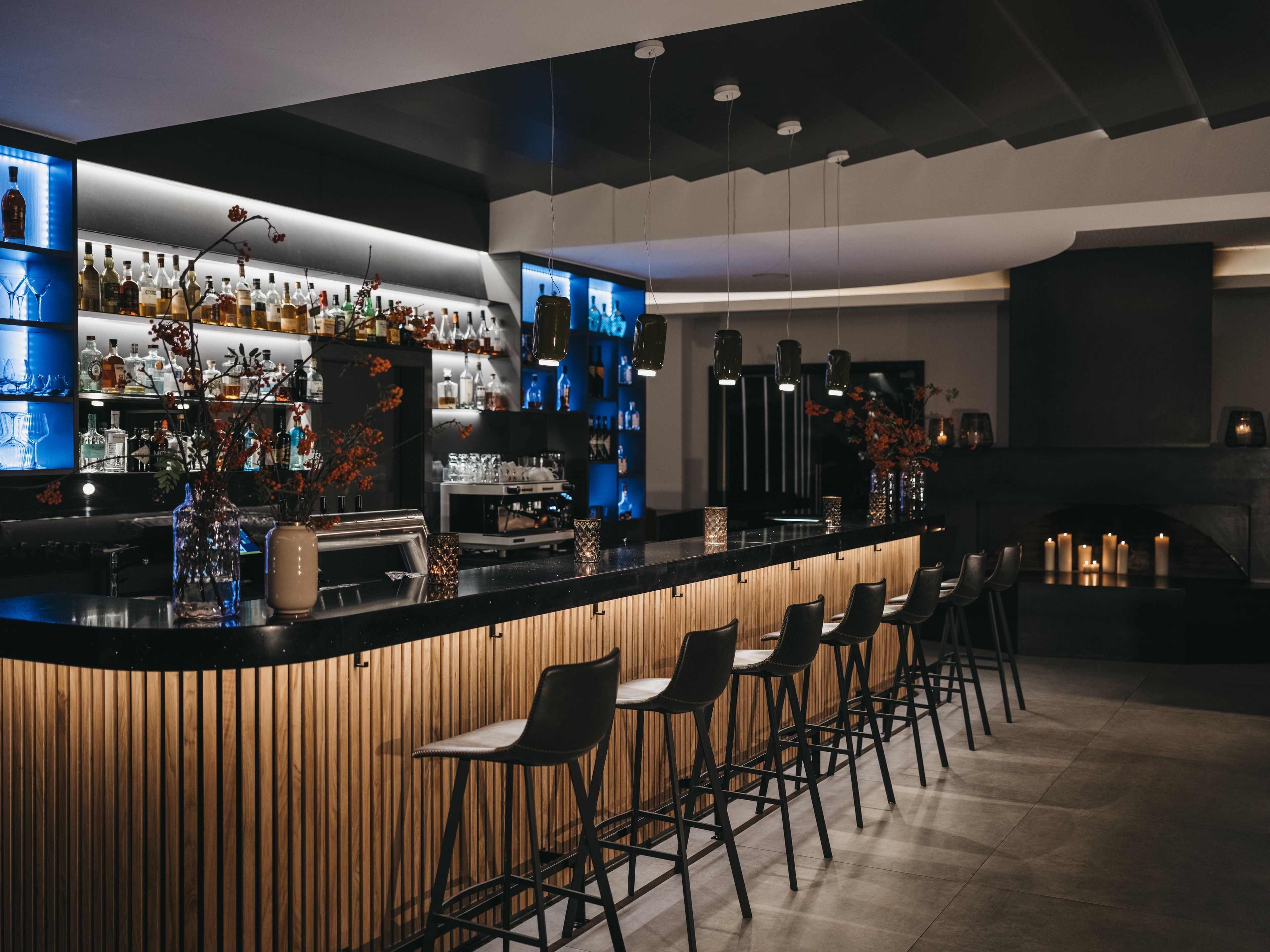 Una zona de bar con una barra larga, varios taburetes y una amplia variedad de botellas y vasos.