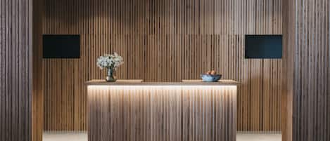 A reception desk with a wooden panel backdrop, a vase with flowers, and a bowl of fruit.