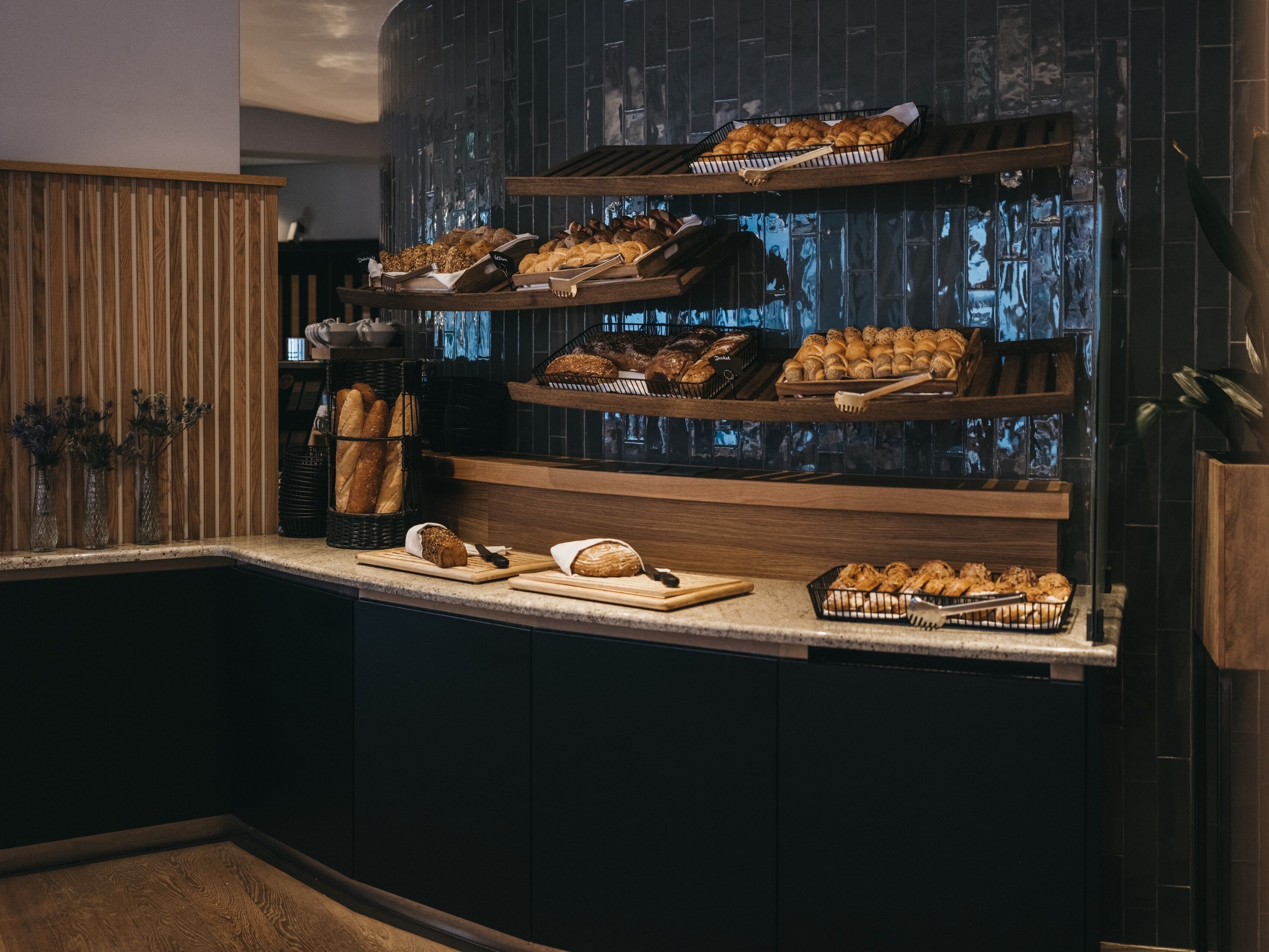 Ein Frühstücksbuffet mit verschiedenen Brotsorten und Gebäck, präsentiert auf Regalen.