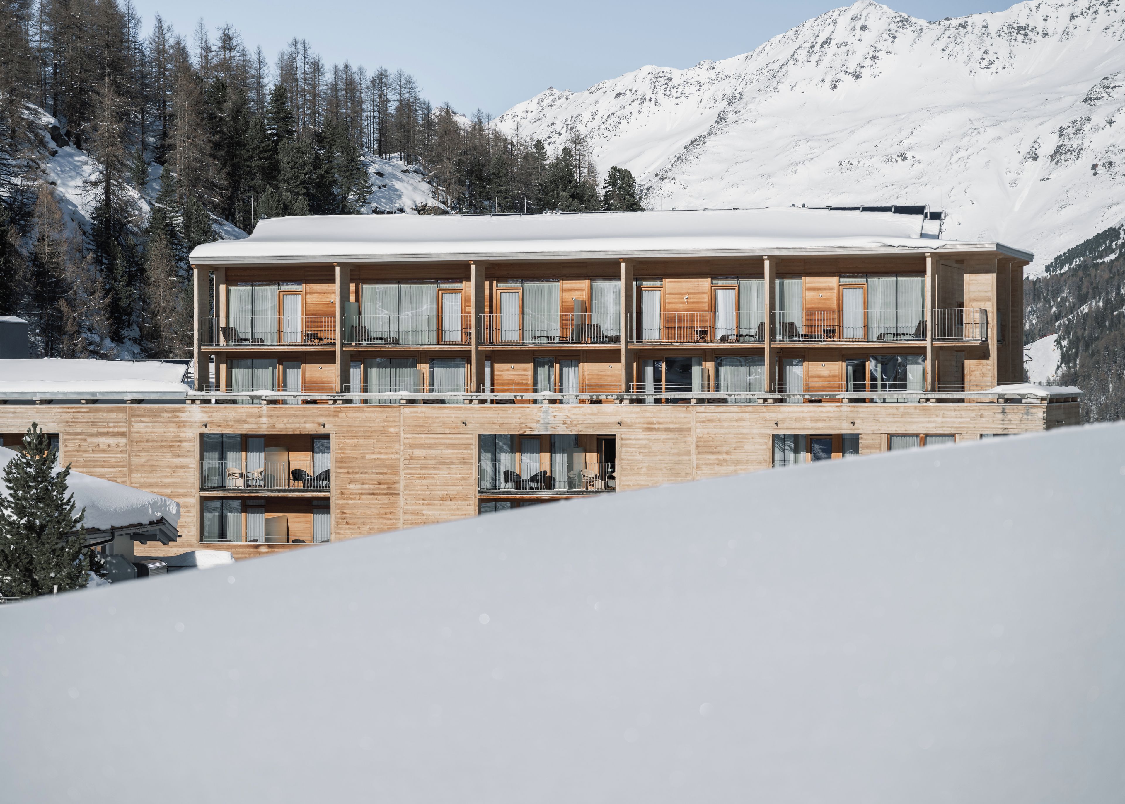 A multi-story wooden building with balconies, set against a snowy mountain backdrop.