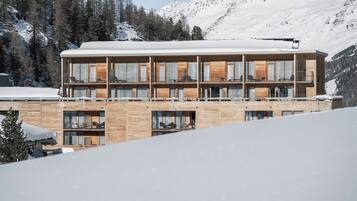 A multi-story wooden building with balconies, set against a snowy mountain backdrop.