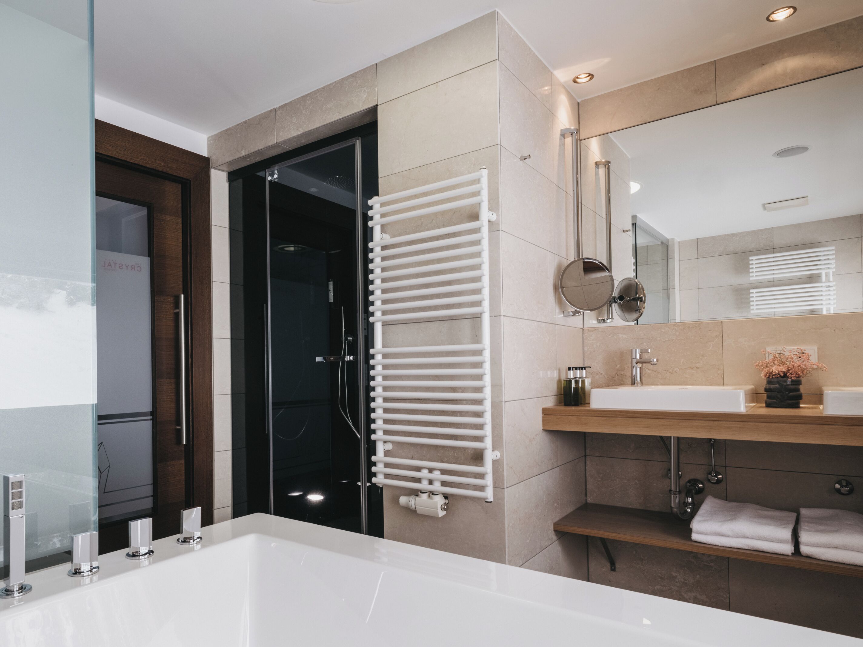 A modern bathroom with a large bathtub, a glass shower enclosure, a white towel rack, and a wooden vanity with a mirror.