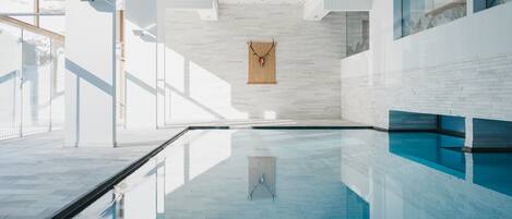 Una piscina interior moderna con paredes de vidrio transparente, suelo de baldosas y puerta de madera.