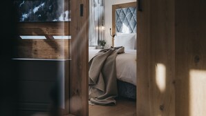 A bedroom with a wooden floor, a bed with a quilted headboard, and a window with a view of trees. - The Crystal VAYA Unique (Obergurgl)