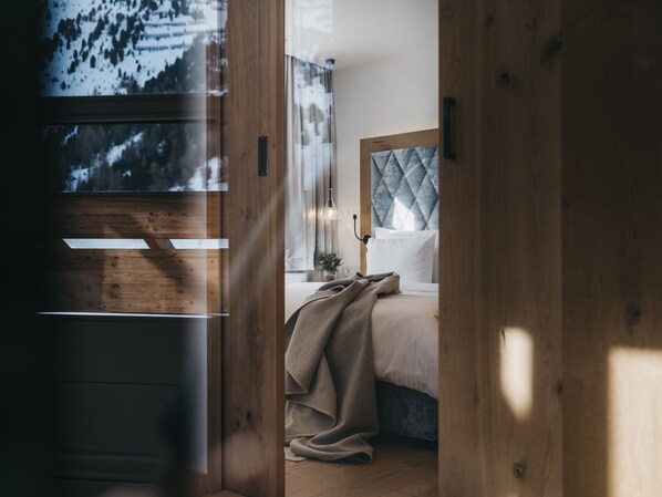 Un dormitorio con suelo de madera, cama con cabecera acolchada y ventana con vistas a árboles.