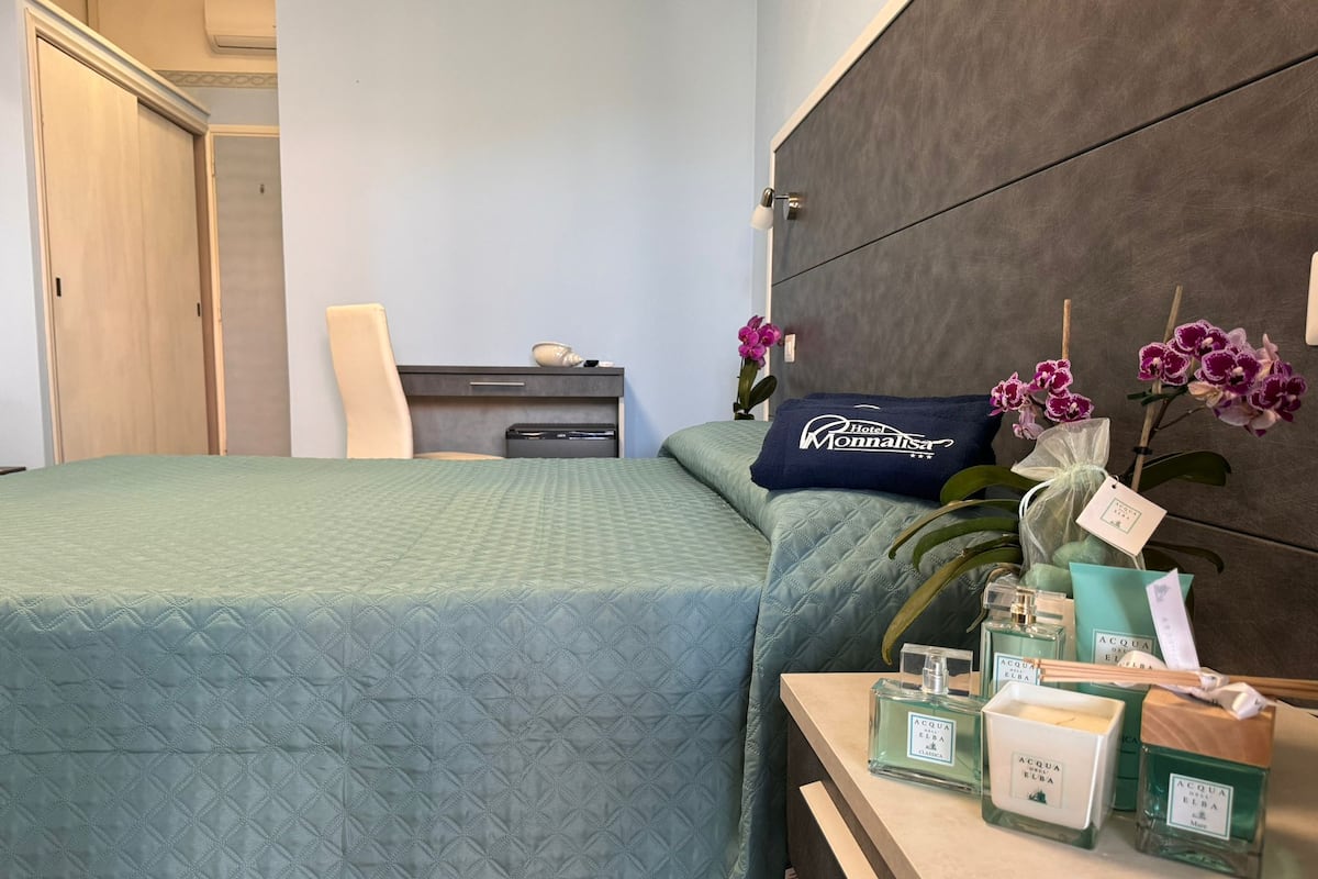 Une chambre d’hôtel comprenant un lit, un bureau, une chaise, une table de chevet avec des articles de toilette et des orchidées.
