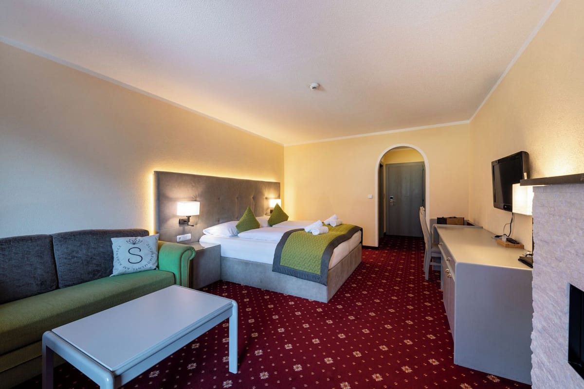 Una habitación de hotel con cama, sofá, escritorio, televisión y chimenea.