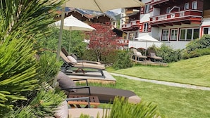 Un hotel con terraza al aire libre, una sombrilla grande y montañas al fondo.
