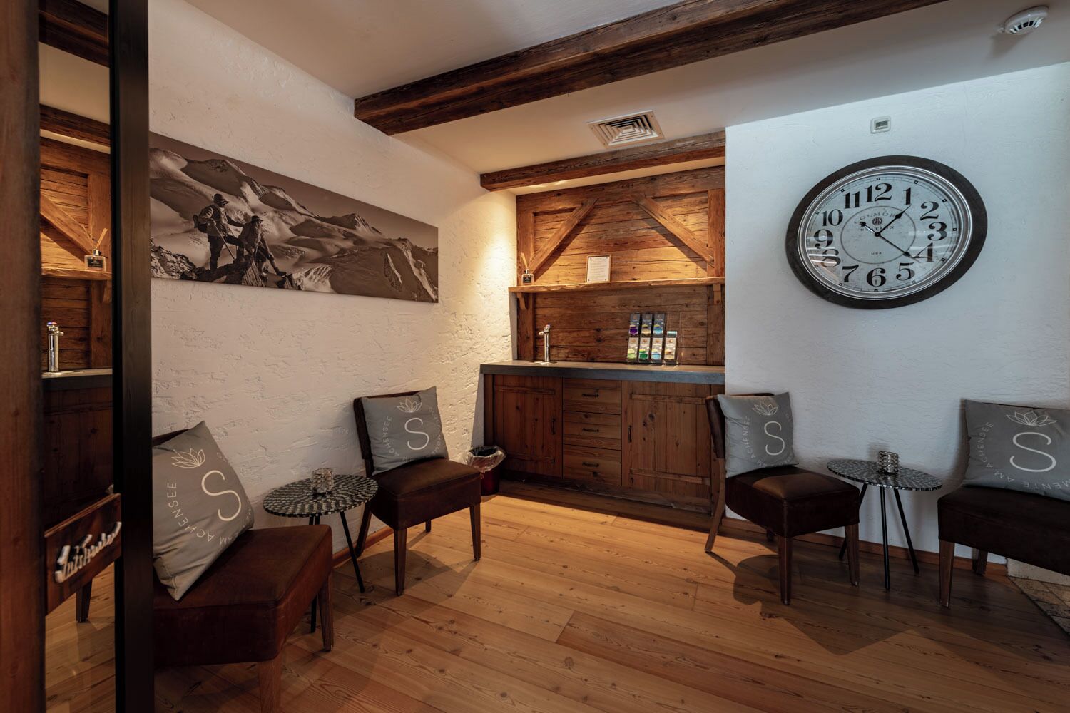 Una habitación acogedora con suelos de madera, un reloj grande y una zona de bar con armarios de madera y un cuadro en la pared.