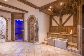 A bathroom with a stone sink, wooden beams, and a blue-lit shower area.