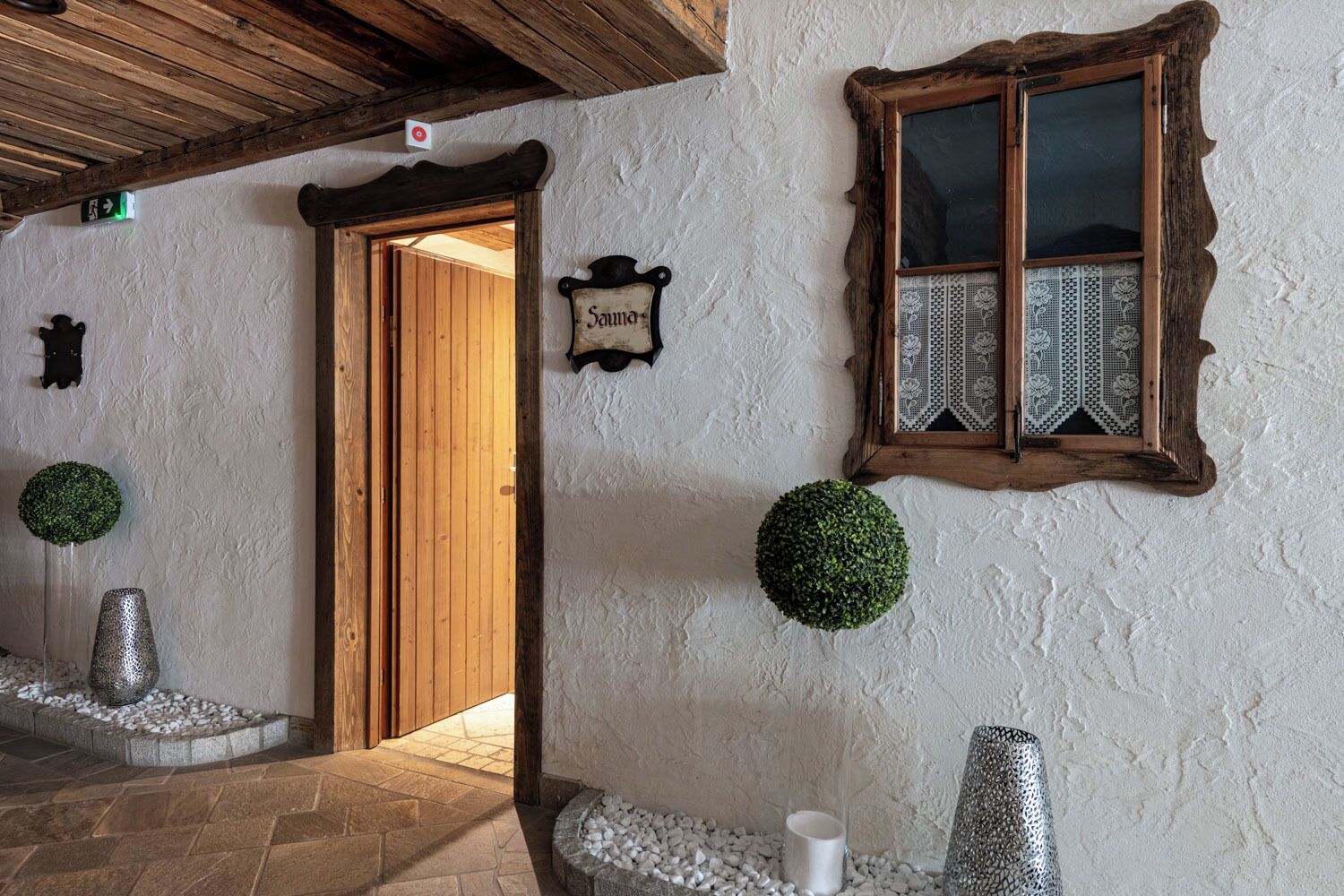 A rustic interior with a wooden door, a sign reading 'Sauna,' and decorative elements like a round green plant and a textured wall.