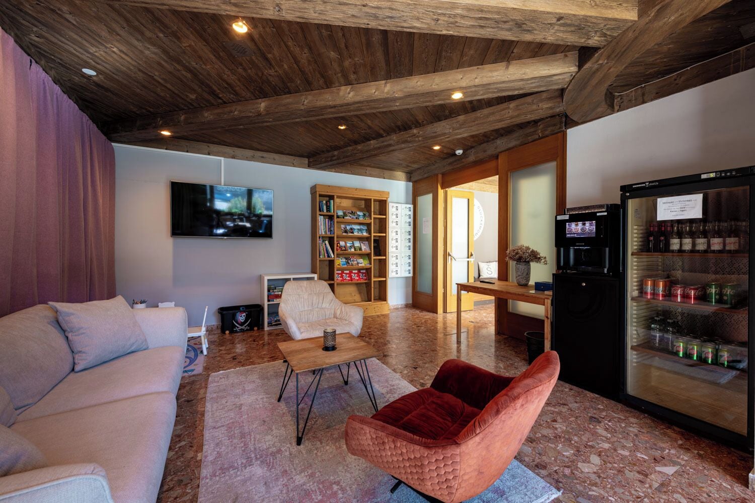 Ein Wohnzimmer mit Sofa, Sessel, Couchtisch, Bücherregal, Fernseher und einem Kühlschrank.