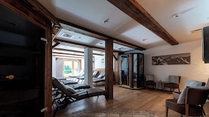 Una habitación amplia con vigas de madera, un ventanal que da al exterior y una zona de estar con sillones reclinables.